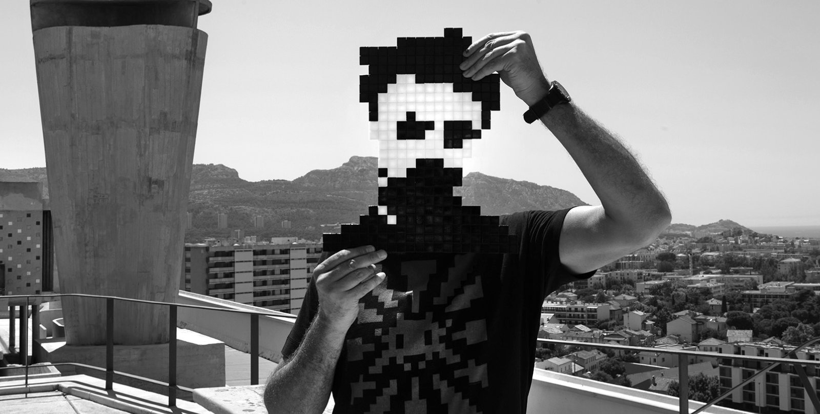 Invader holding a pixelated artwork in front of his face, as pictured in HENI’s press kit