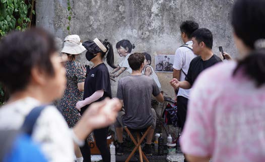 Ernest Zacharevic restoring his Kids on Bicycle mural in George Town in 2024, with visitors passing nearby