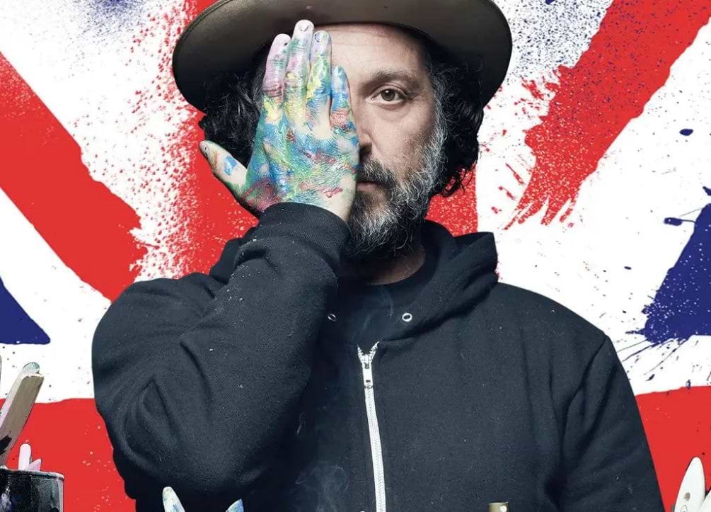 Mr. Brainwash wearing a black hat, with a paint-covered hand over one eye.