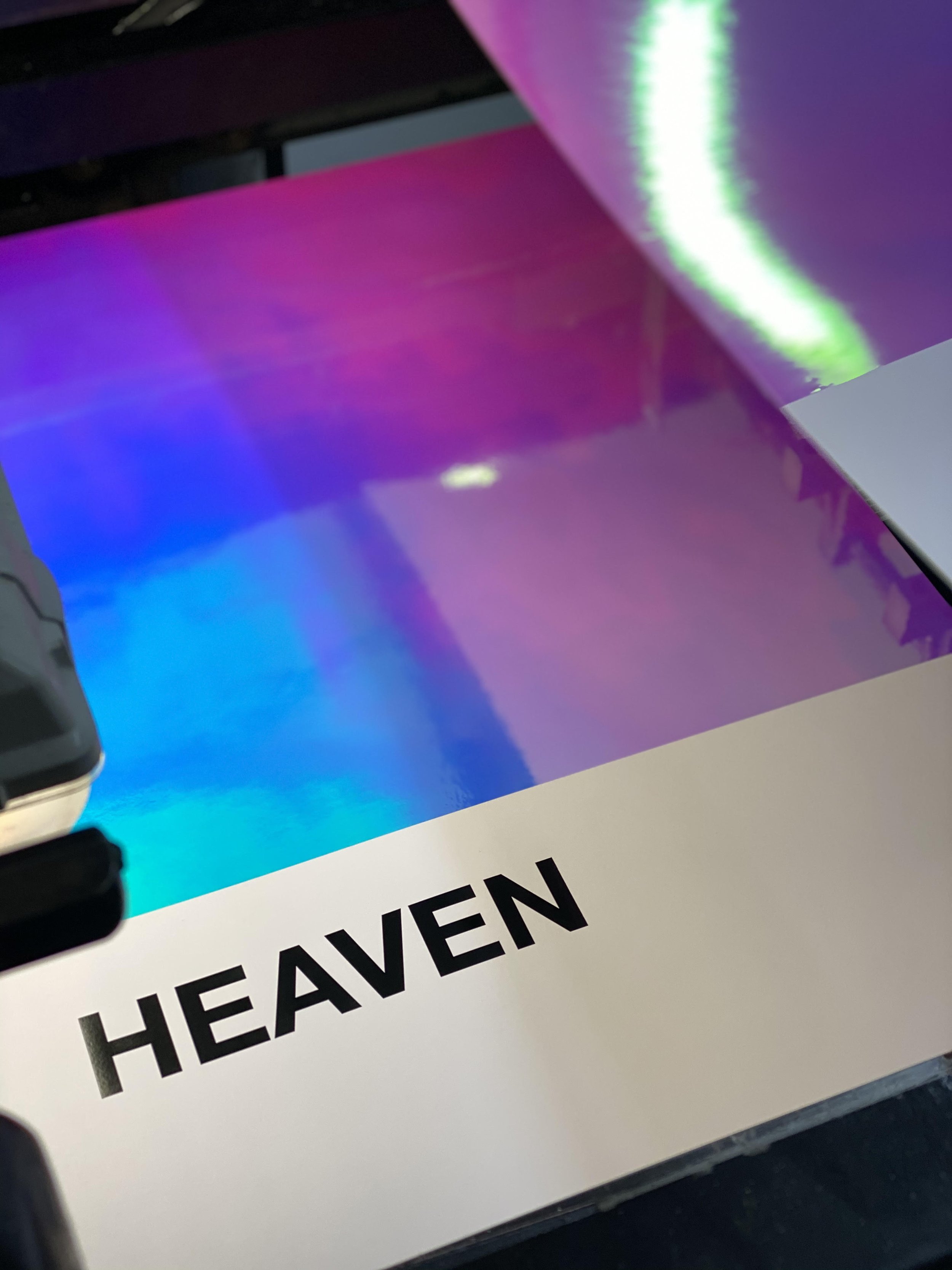 Artist-supplied detail photograph of Nick Smith’s HEAVEN foil-and-letterpress edition, showing its iridescent upper field and black title on white paper.