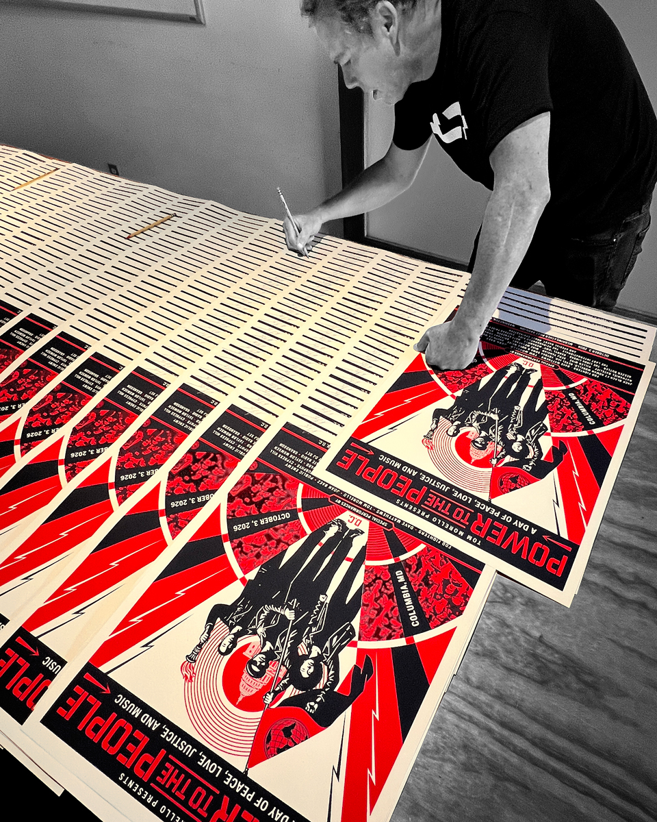 Shepard Fairey leans over a table to sign rows of Power to the People Festival prints.